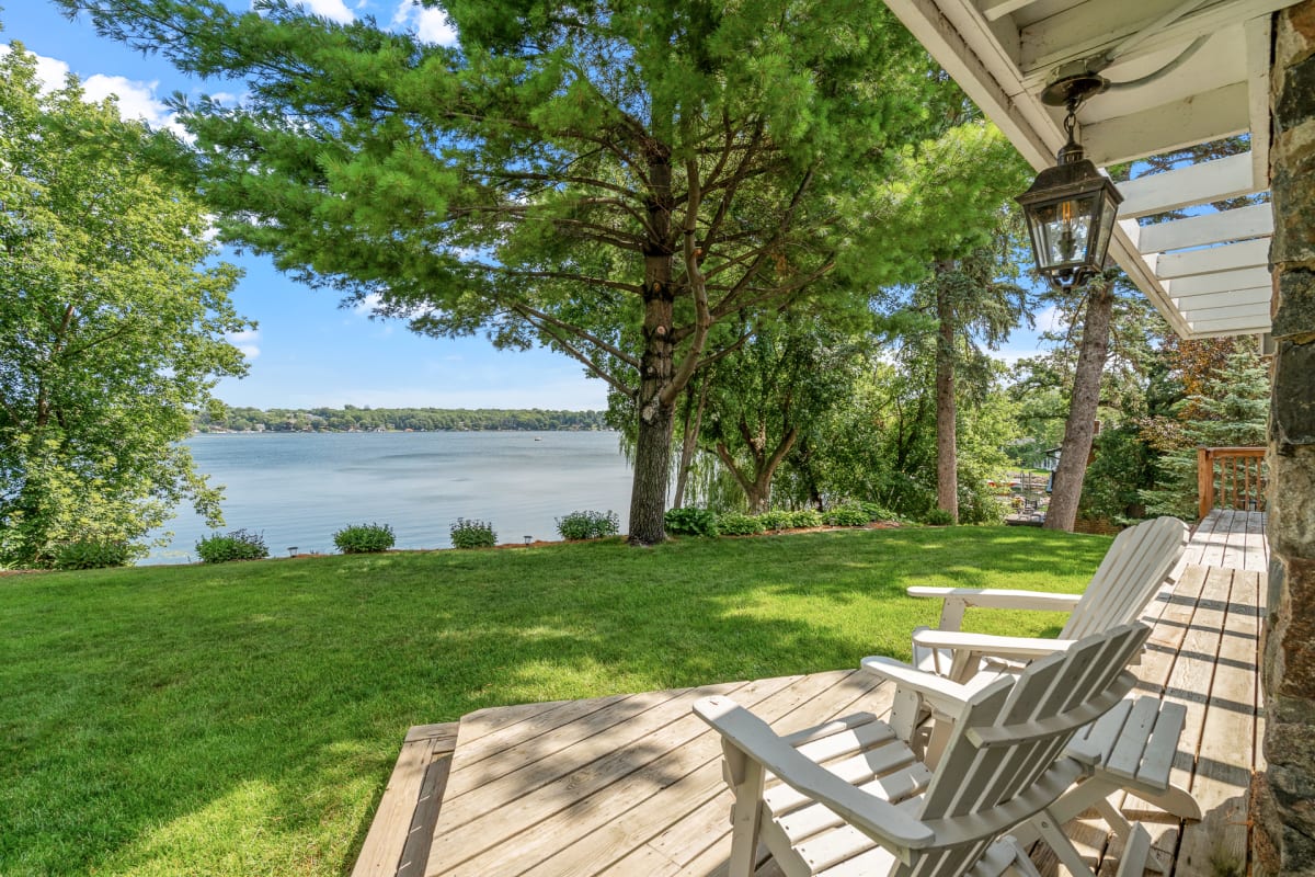 A tranquil lakeside view from a wooden deck with Adirondack chairs.