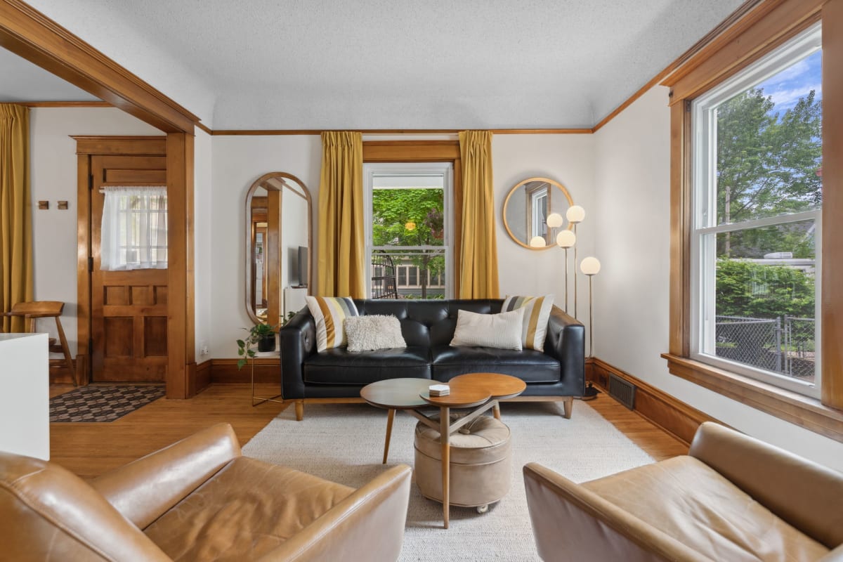 A stylish living room featuring a black leather sofa and yellow curtains, with warm wooden accents.