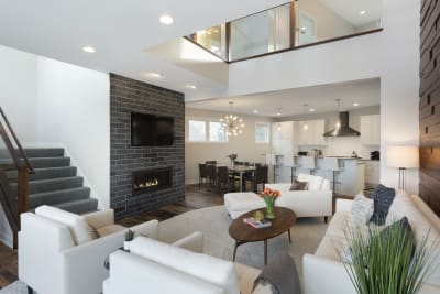 A contemporary living room with white sofas, a stone fireplace, and a dining area in an open plan layout.