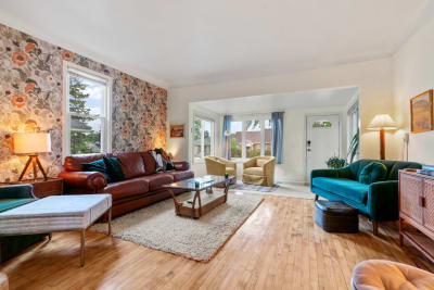 A bright living room with floral wallpaper, brown leather sofa, teal accents, and natural light.