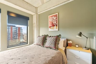 Modern bedroom featuring olive green walls, a comfortable bed, and urban landscape views.