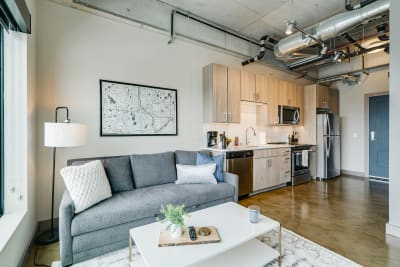 Interior view of a modern apartment showcasing a gray couch, coffee table, kitchen, and decorative map on the wall.