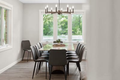 Modern dining room with a wooden table, elegant chairs, and a chandelier, surrounded by windows.