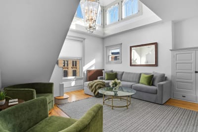 Bright living room with skylights, gray sectional sofa, and green accent chairs.