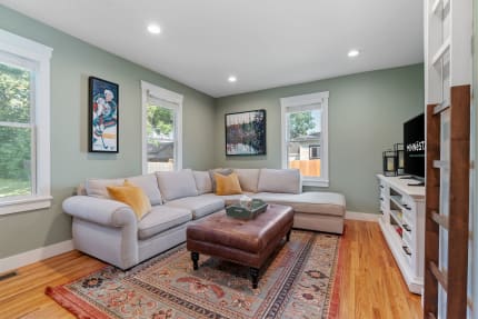 A living room featuring a grey sectional sofa, leather ottoman, and decorative artwork on green walls.