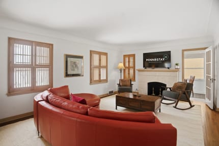 Bright living room featuring a red leather sofa, wooden windows, and a mounted TV.