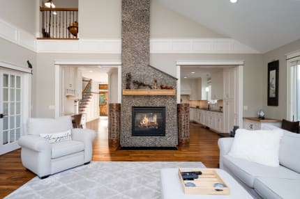 Modern living room with a stone fireplace, white furniture, and an open kitchen view.