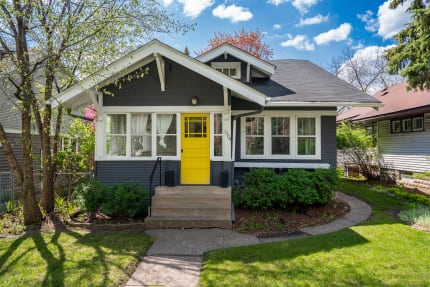 Charming cottage with a yellow door and lush greenery in a residential area.