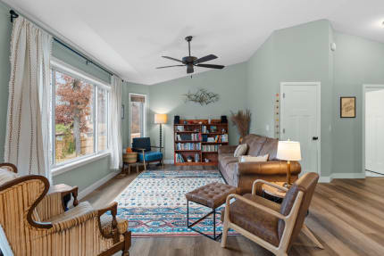 Cozy living room with large windows, brown leather couch, bookshelf, and blue armchair.