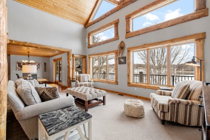A spacious living room featuring high wooden ceilings, large windows, and rustic furniture.
