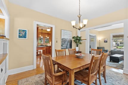 A cozy dining room connected to a kitchen, showcasing a wooden dining table, chandelier, and artwork.