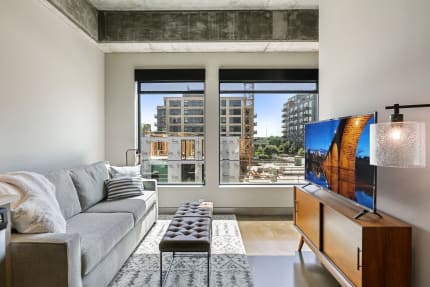 Modern living room featuring a grey sofa, a wooden media console, and a view of an urban construction site outside.