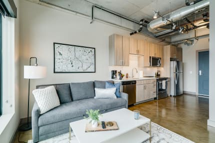 Interior view of a modern apartment showcasing a gray couch, coffee table, kitchen, and decorative map on the wall.