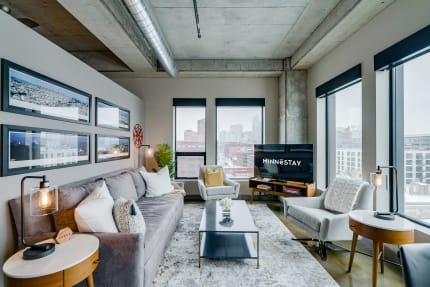 Modern urban living room with a gray sofa, large windows, and city skyline view.