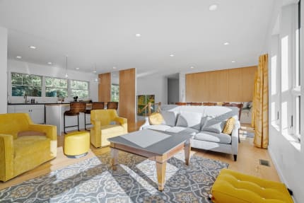 Bright living area featuring yellow chairs, gray sofa, and a modern kitchen backdrop.