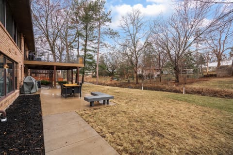 Backyard view showing a patio, deck, and grass area with trees in the background.