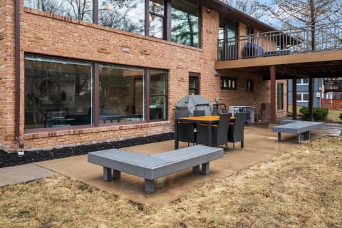 An outdoor patio area with a dining table, grill, and modern brick house in the background.