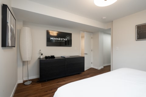 Interior view of a modern hotel room with a floor lamp, dark cabinet, and flat-screen TV.