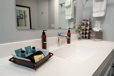 Modern bathroom countertop with a white sink, brown tray of personal care items, and decorative elements.