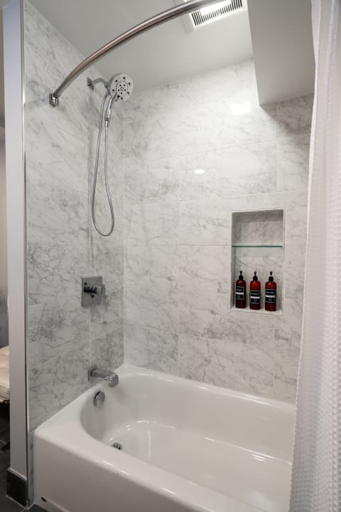 Modern bathroom with a marble-tiled shower and tub, featuring a sleek showerhead and organized toiletries.