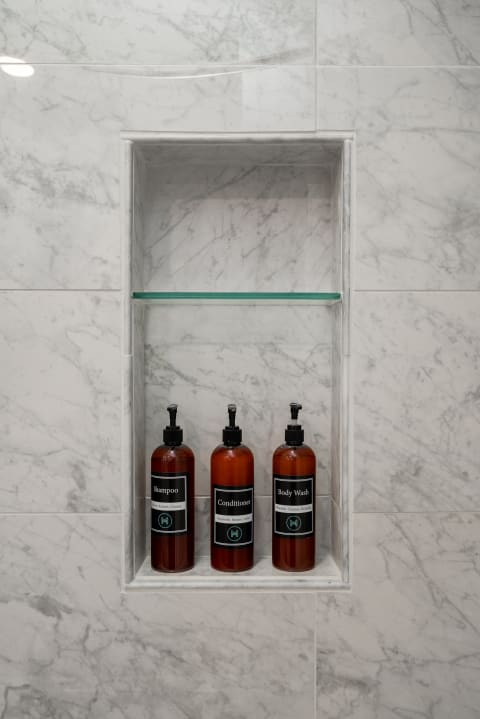 Modern shower shelf displaying shampoo, conditioner, and body wash bottles against a marble background.