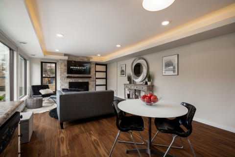 A modern living room with a gray sofa, round white dining table with apples, and a stone fireplace.