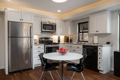 A contemporary kitchen with white cabinetry, stainless steel appliances, and a circular dining table with red apples.