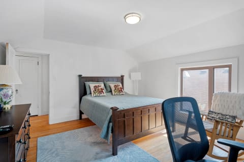 A bright and cozy bedroom featuring a wooden bed, colorful pillows, and a rocking chair.
