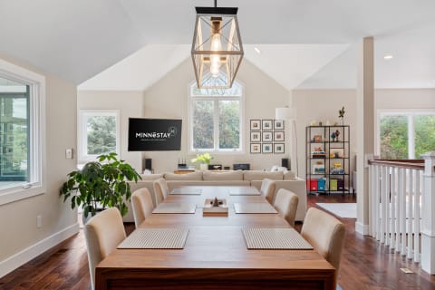 Stylish and modern dining area with a long table, beige chairs, and a cozy living space.