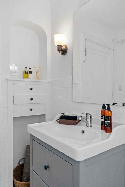A modern bathroom featuring a white sink, gray cabinetry, and warm lighting.