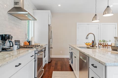 A modern kitchen with granite countertops, stainless steel appliances, and colorful mugs.