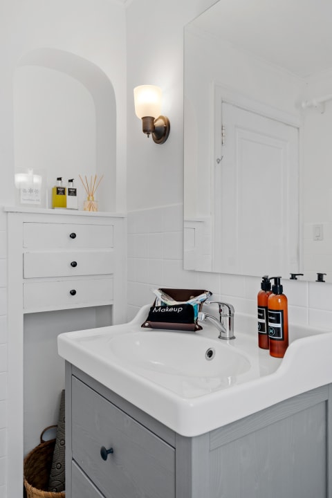 A bright minimalist bathroom with a sink, lighted mirror, and neatly arranged toiletries.