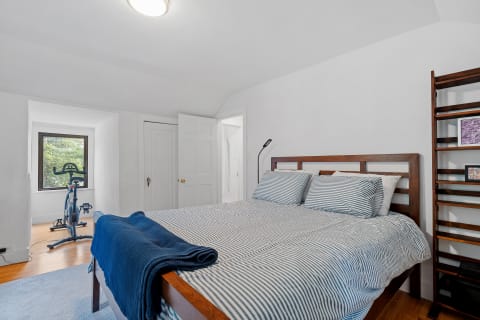 Cozy bedroom featuring a wood bed with striped bedding and an exercise bike by the window.
