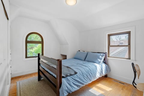 Bright bedroom featuring a wooden bed, striped bedding, and large windows.