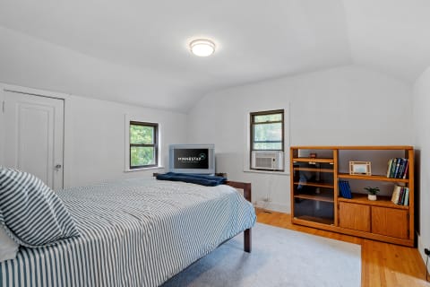 Cozy bedroom with striped bedding, wooden shelf, and air conditioning unit.