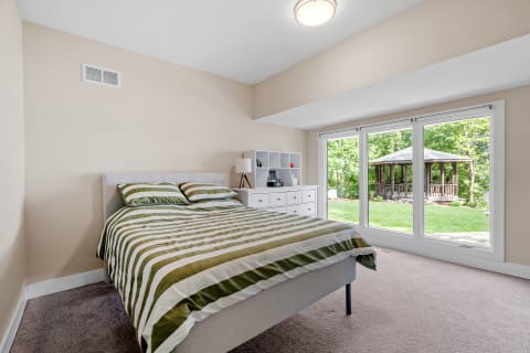 A modern bedroom featuring stripes on the bedspread and large windows looking out to a gazebo.