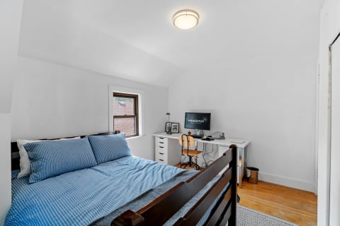 Minimalist bedroom with a bed, desk, and computer monitor.