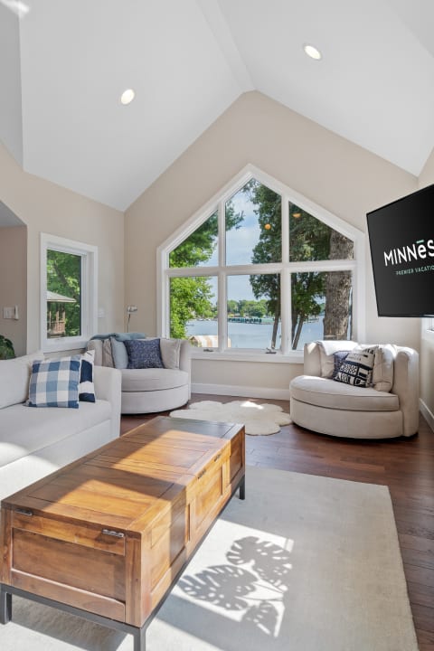 Comfortable living room with large windows overlooking a lake, featuring a wooden coffee table and soft seating.