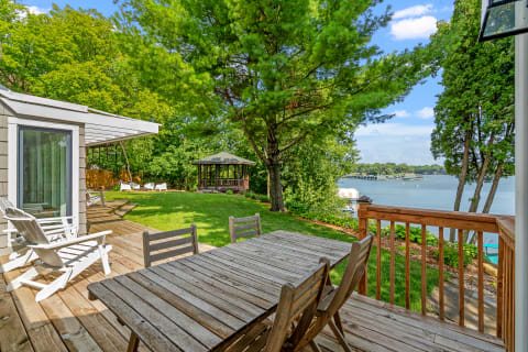 Wooden deck overlooking a lake with a gazebo and green grass.