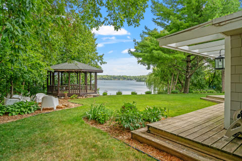 A peaceful landscape with a gazebo by the lake and green lawn.