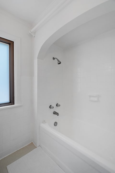 A clean, white bathroom featuring a bathtub and showerhead, illuminated by natural light.