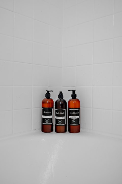 Amber bottles of shampoo, body wash, and conditioner placed in a white-tiled shower.
