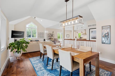 A stylish dining area with a wooden table, upholstered chairs, and a modern light fixture, seamlessly connected to a living space.