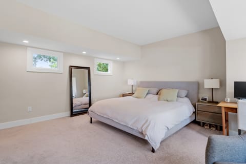 A modern bedroom with a large bed, mirror, and desk, exuding a calm vibe.
