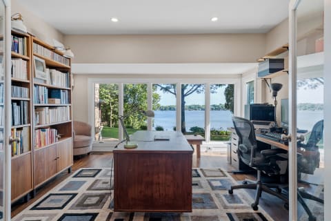 An elegant home office with a desk, bookshelves, and a view of the lake through large windows.