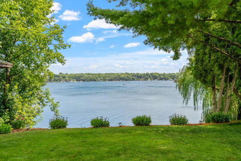 A peaceful view of a lake surrounded by trees and green grass under a blue sky.