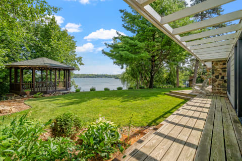 Lakeside view with a deck, gazebo, and green landscaping.