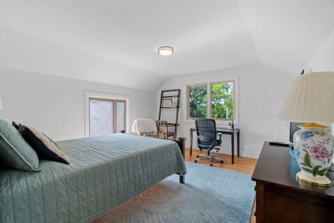 A serene bedroom with a bed, desk, and large window looking out to greenery.