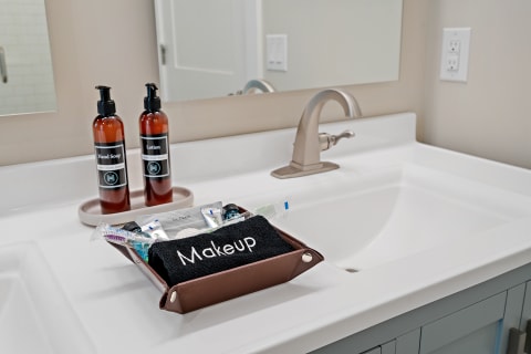 Modern bathroom countertop with hand soap, lotion, and makeup items in a tray.