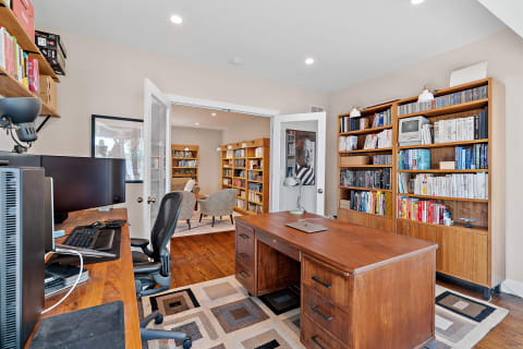 A stylish home office featuring a wooden desk, ergonomic chair, and two bookshelves in a brightly lit space.